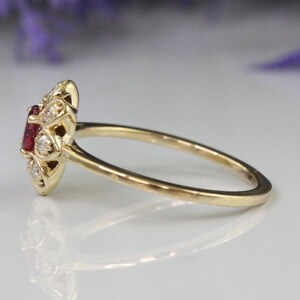 May include: A gold ring with a red gemstone surrounded by smaller white gemstones.