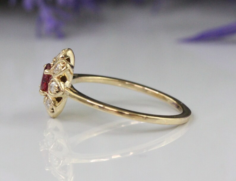 May include: A gold ring with a red gemstone surrounded by smaller white gemstones.