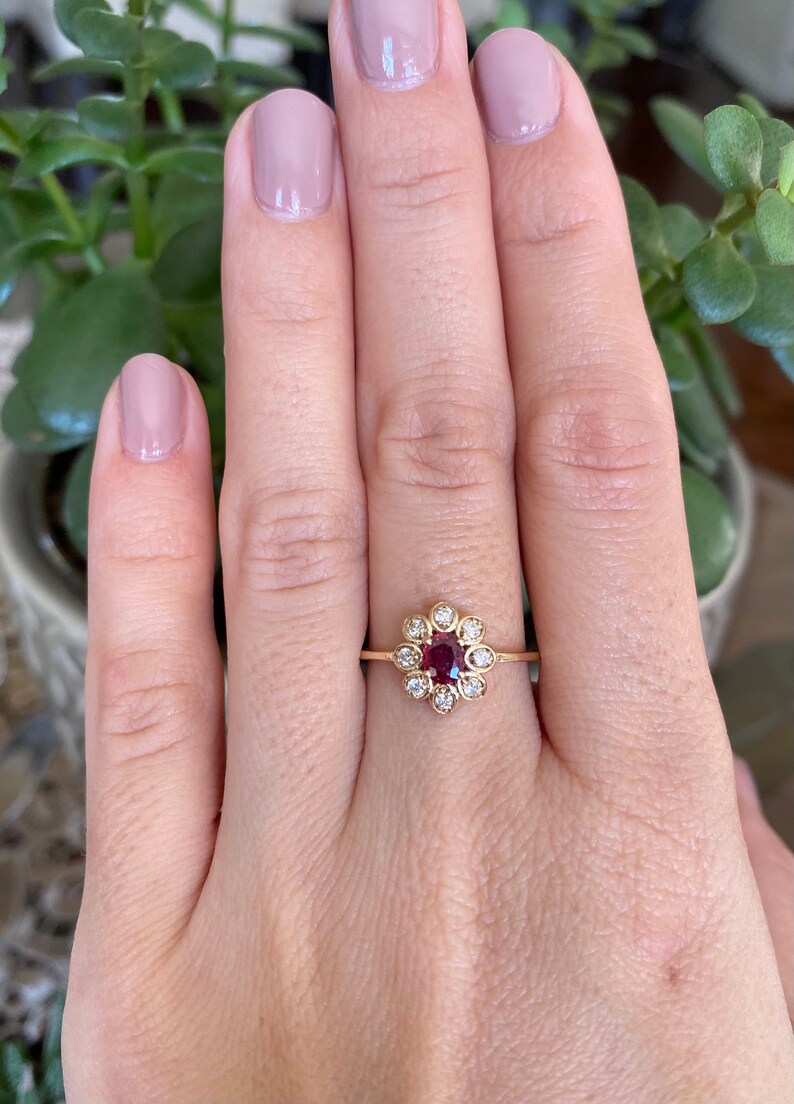 May include: A gold ring with a red gemstone surrounded by smaller white gemstones, set in a flower-shaped design.