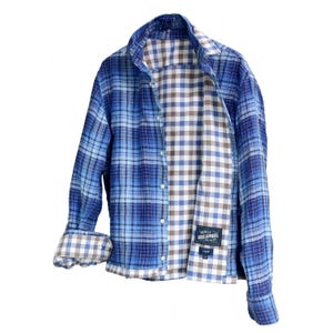 Könnte beinhalten: Blau kariertes Hemd mit einem kontrastierenden braun-weiß karierten Innenfutter. Das langärmlige Hemd hat einen klassischen Kragen und eine Knopfleiste. Das Etikett lautet "REALEY BOSS APPAREL".