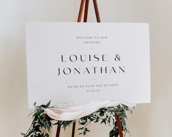 May include: A white sign with black text on a wooden easel. The sign reads "Welcome to our wedding, Louise & Jonathan, We're so glad you're here, 23.03.23".