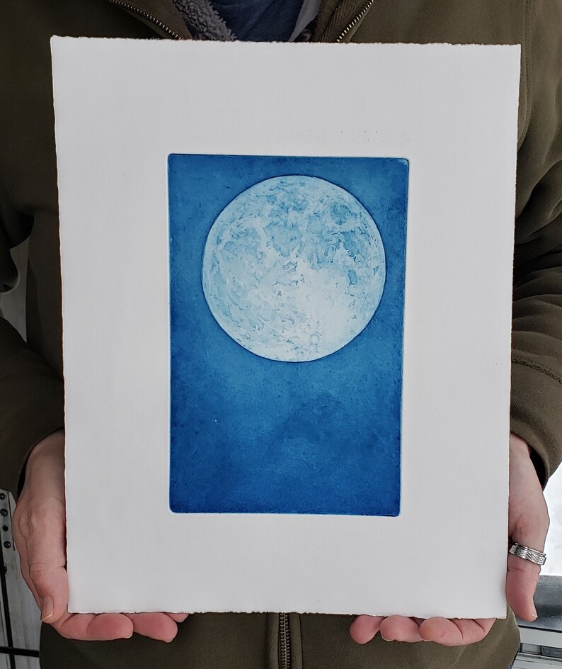 May include: A blue and white print of a full moon on a white background.