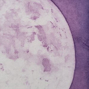 May include: A close-up of a watercolor painting of a purple moon. The moon is painted in shades of purple and white, with a textured surface.