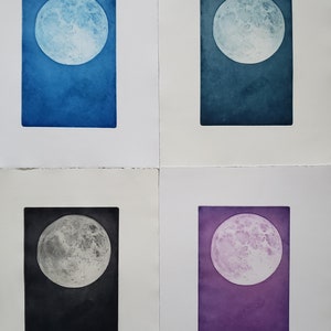 May include: Four different colored prints of the full moon. Each print is framed in a white mat and has a white border. The moon is depicted in shades of blue, teal, gray, and purple.