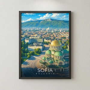 May include: A framed wall art print depicting an aerial view of Sofia, Bulgaria, featuring the Alexander Nevsky Cathedral with its prominent gold dome and green roofs, set against a backdrop of mountains under a bright blue sky with white clouds.