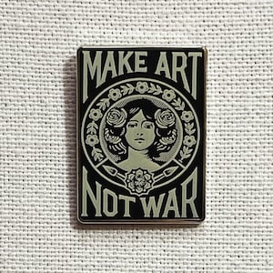 May include: A black and white enamel pin with a woman's face surrounded by flowers and the text "MAKE ART NOT WAR".