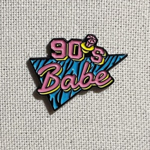 May include: A blue and pink enamel pin with a 90's Babe design. The pin features a diamond ring and a zebra print background.