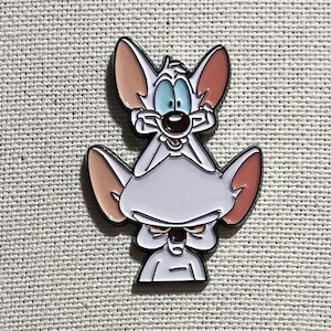 Könnte beinhalten: Eine weiße Emaille-Anstecknadel mit einer Cartoon-Maus mit großen Ohren und einem überraschten Ausdruck. Die Maus ist auf einer anderen Maus mit einem mürrischen Ausdruck gestapelt.