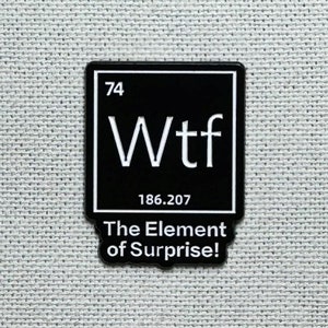 May include: A black and white enamel pin with the word "Wtf" in a periodic table style. The pin also includes the number "74" and "186.207". Below the word "Wtf" is the text "The Element of Surprise!"