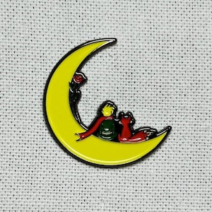May include: A yellow crescent moon enamel pin with a small red rose, a figure in a green jacket and red scarf, and a fox in red and orange.