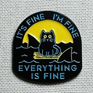 May include: Black enamel pin featuring a black cat perched on a shark fin. The cat has yellow eyes and the background is yellow. The text surrounding the cat reads "It's Fine I'm Fine Everything Is Fine".