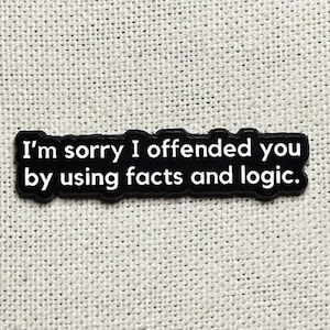 Pode incluir: Um patch retangular preto com o texto branco "I'm sorry I offended you by using facts and logic". O patch está centrado em um fundo de tecido bege claro.