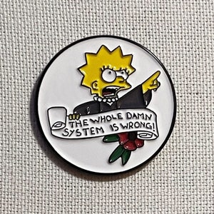 Op de afbeelding: Ronde emaille pin met Lisa Simpson uit The Simpsons. Lisa wijst naar een rol met de tekst "THE WHOLE DAMN SYSTEM IS WRONG!". De pin heeft een witte achtergrond, een zwarte rand en een rode roos.