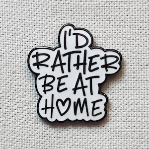 Könnte beinhalten: Weißer Emaille-Pin mit schwarzem Umriss. Der Pin sagt "I'd rather be at #♥ome".