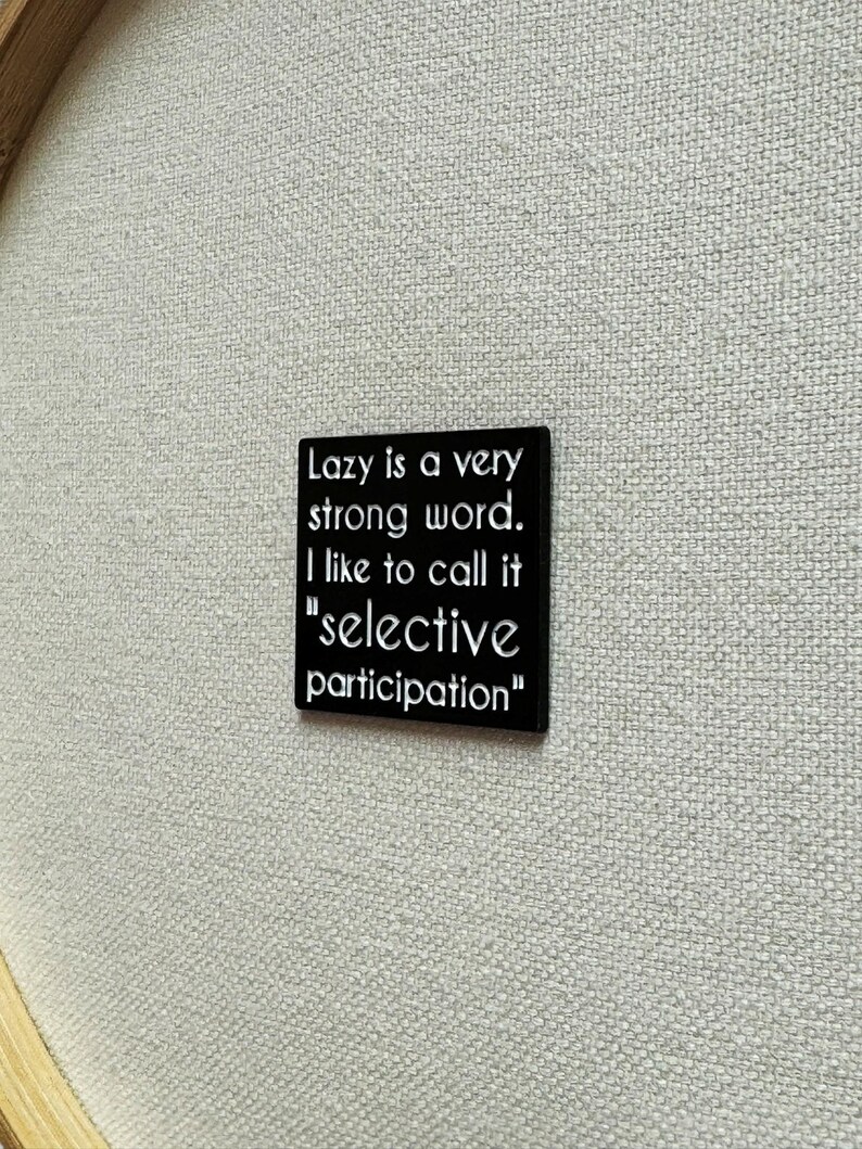 May include: Black square pin with white text that reads "Lazy is a very strong word. I like to call it "selective participation""