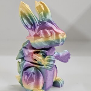 May include: A rainbow-colored 3D printed rabbit figurine with a textured surface. The rabbit is standing on all four legs and has its arms raised.