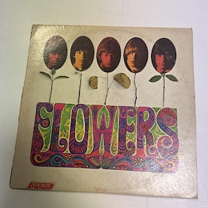 May include: A square vinyl record jacket titled Flowers by The Rolling Stones. The cover features five oval portraits of band members atop thin stems with leaves, above the word FLOWERS in colorful, intricate, psychedelic-style lettering.