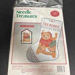 May include: A sealed package for a counted cross stitch kit. The kit features a Christmas stocking design with a teddy bear in a chair, the name "THEODORE", and the text "MERRY CHRISTMAS". The kit includes a free ornament.