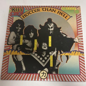 May include: Album cover for the band KISS, titled "Hotter Than Hell." The cover features four band members in makeup and costumes. The background is a mix of colors, with text in English and Japanese. The album is in a red and silver striped border.