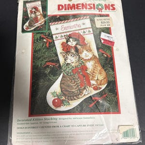 May include: A Dimensions needlepoint kit for a 16-inch Christmas stocking titled Decorated Kitties Stocking. The packaging features an illustration of three cats wearing holiday accessories, with the name Samantha printed at the top.