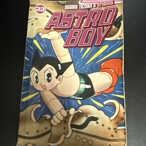 May include: Astro Boy comic book cover featuring the character in a dynamic pose. The cover has a blue and tan background with the title "Astro Boy" in a red and white font. The text "Osamu Tezuka's original" is also visible.