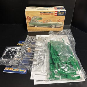 May include: A model kit of a 1959 Ford Fairlane 500 Skyliner with a retractable top. The box features an illustration of the car in green. The kit includes plastic parts, wheels, and instructions. The Revell brand is visible.