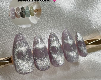 May include: Set of six long, oval-shaped, silver glitter press-on nails with a light purple base.  The nails have a holographic effect.  "Select the color" is written in the image.