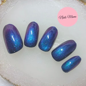 May include: Oval-shaped, iridescent nail enhancements in shades of blue and purple. The nails have a glossy finish and a subtle shimmer. The image includes the text "Nails Momo" in a pink circle.