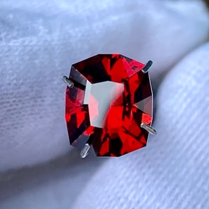 May include: A deep red gemstone with a faceted cut, held in place by prongs. The gemstone is a vibrant red colour and has a high level of brilliance.