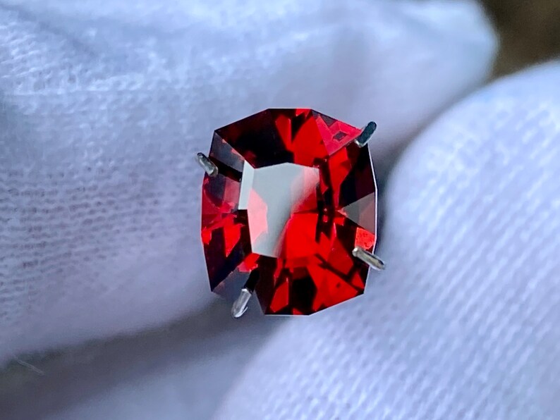 May include: A deep red gemstone with a faceted cut, held in place by prongs. The gemstone is a vibrant red colour and has a high level of brilliance.