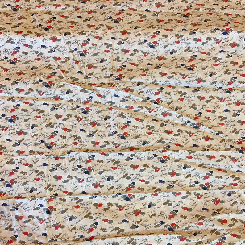 May include: A white fabric with a repeating pattern of small, stylized brown, red, and blue shapes. The fabric has a slightly wrinkled texture.