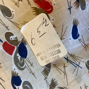 May include: A close-up of a fabric care label with the text "65% Polyester 85% Cotton RN51869". The label is attached to a beige fabric with a pattern of stylized birds.