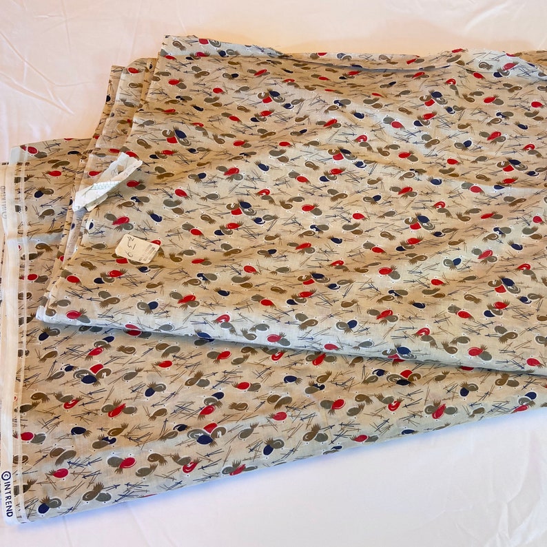 May include: Beige fabric with a repeating pattern of red, blue, and gray stylized leaves. The fabric is folded in half and the edges are visible.