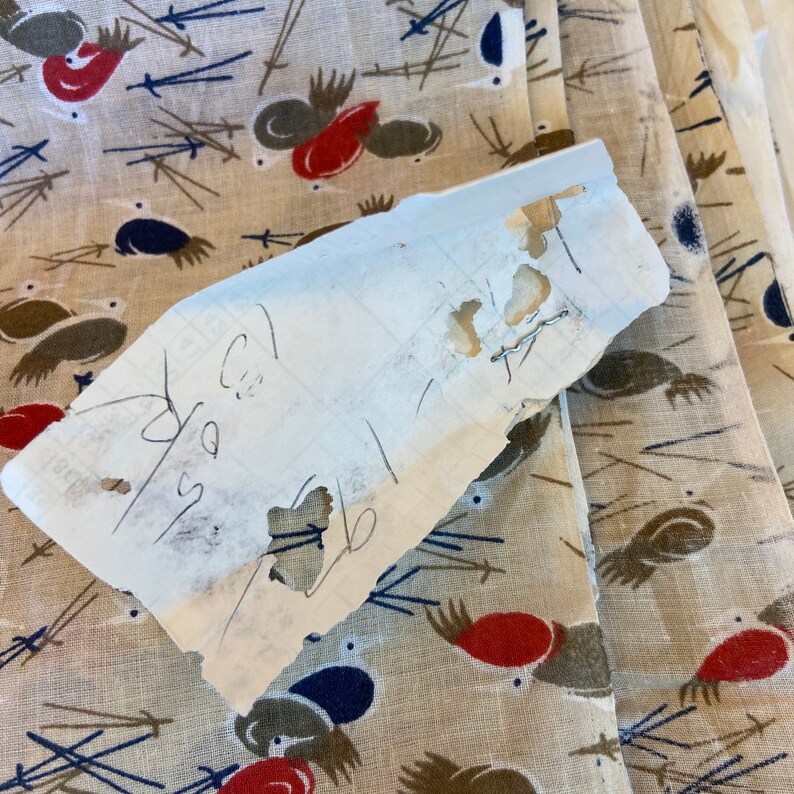 May include: A piece of white paper with handwritten notes and holes. The paper is lying on top of a beige fabric with a repeating pattern of brown, red, and blue birds.