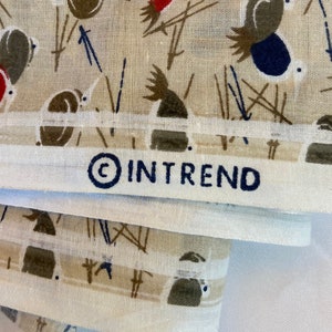 May include: A stack of white fabric with a brown and black pattern of stylized birds and geometric shapes. The fabric has a white border and the text "&copy; IN TREND" printed in black.