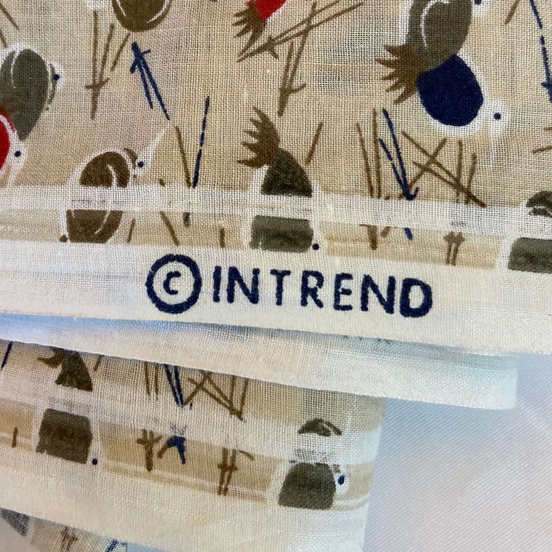 May include: A stack of white fabric with a brown and black pattern of stylized birds and geometric shapes. The fabric has a white border and the text "&copy; IN TREND" printed in black.