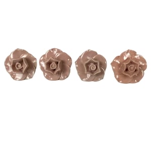 May include: Four ceramic rose-shaped knobs in a pale pink color. The knobs have a raised, detailed rose design.