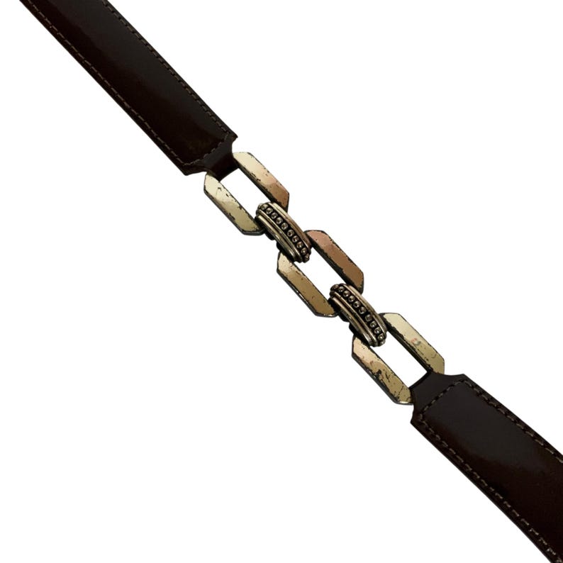 May include: A brown belt with a metallic chain-link clasp. The belt has a glossy finish and a rectangular buckle. The chain links are silver and have small, decorative embellishments.
