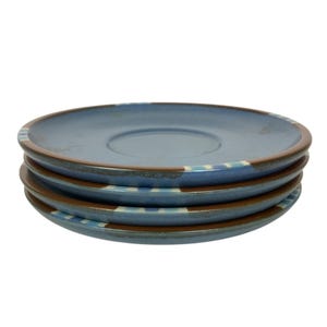 以下が含まれることがあります： 茶色の縁と水色と白のストライプ模様が施された、4枚の青いセラミックプレートのスタック。 プレートの中央はわずかにくぼんでおり、互いの上に積み重ねられています。