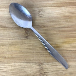May include: A silver spoon with a star design on the handle. The spoon is on a wooden surface.