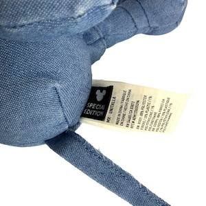 May include: A blue denim-textured plush toy with a white fabric tag attached. The tag features a black Mickey Mouse icon, the text SPECIAL EDITION, and lists material composition as 88% polyester, 10% plastic fibres, and 1% polyethylene.