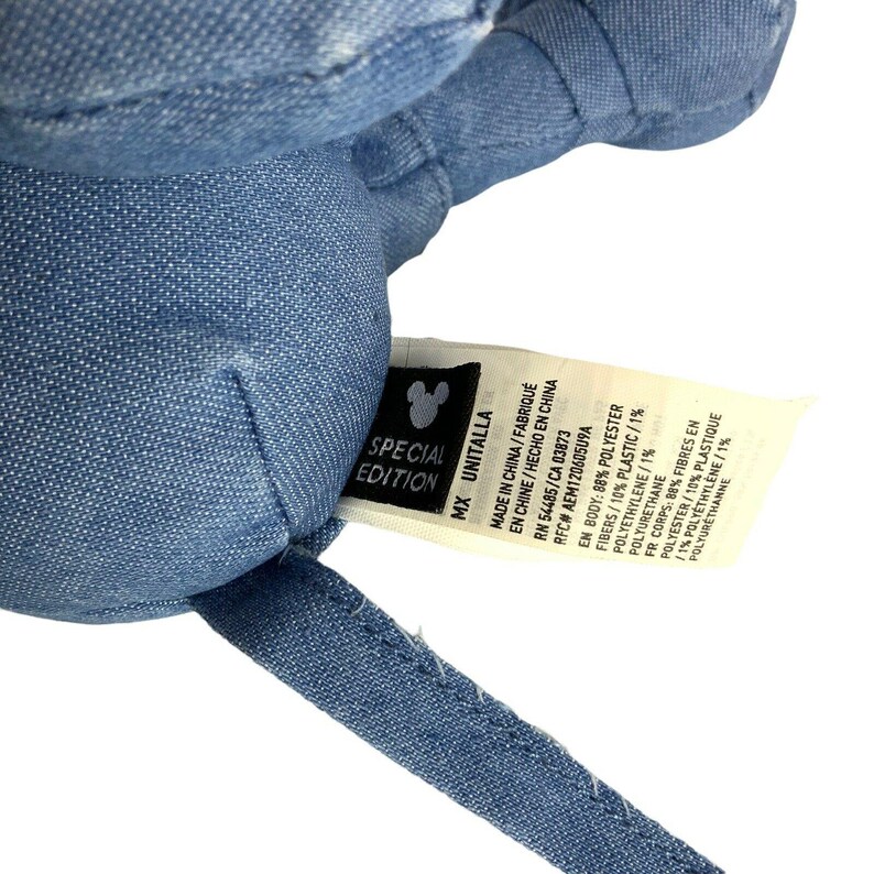 May include: A blue denim-textured plush toy with a white fabric tag attached. The tag features a black Mickey Mouse icon, the text SPECIAL EDITION, and lists material composition as 88% polyester, 10% plastic fibres, and 1% polyethylene.