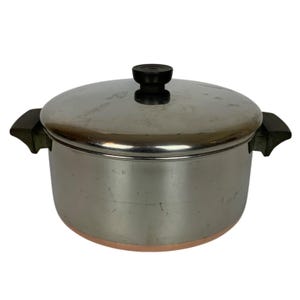 Pode incluir: Uma panela de cozinha em aço inoxidável com tampa e duas pegas laterais. A panela tem uma base de cor cobre e uma pega preta na tampa. A panela foi concebida para cozinhar e preparar alimentos.