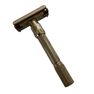 Puede incluir: Una maquinilla de afeitar de seguridad plateada vintage con un mango texturizado y ajustes ajustables. La maquinilla presenta un diseño clásico con un cabezal giratorio y un dial para ajustar la exposición de la cuchilla. El mango está intrincadamente detallado.