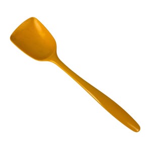 May include: A solid mustard yellow kitchen spatula with a wide, flat, rectangular head and a long, smooth, tapered handle. The utensil features a uniform, glossy finish throughout its entire surface, showcasing a simple, functional design.
