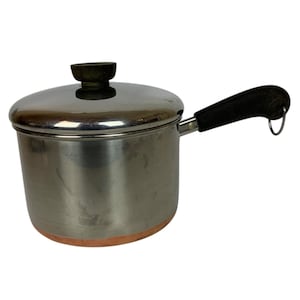 May include: A stainless steel saucepan with a lid and a black handle. The pot has a copper-colored bottom and a black knob on the lid. The handle has a loop at the end. The pot is designed for cooking.