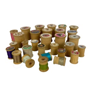 Puede incluir: Una colección de carretes de hilo de coser de madera vintage de varios tamaños, con hilo de colores en tonos morado, marrón, azul claro, turquesa y verde. Cada carrete tiene una etiqueta de papel circular con nombres de marcas y texto.
