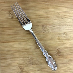 May include: A silver fork with a decorative handle. The fork has four tines and a long, slender handle with an ornate design.