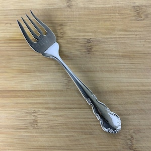 May include: A silver fork with a decorative handle. The fork has four tines and a rounded handle with a floral design.