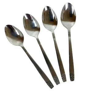 Puede incluir: Cuatro cucharas de plata con diseños ornamentados en los mangos. Las cucharas están dispuestas en forma de abanico.
